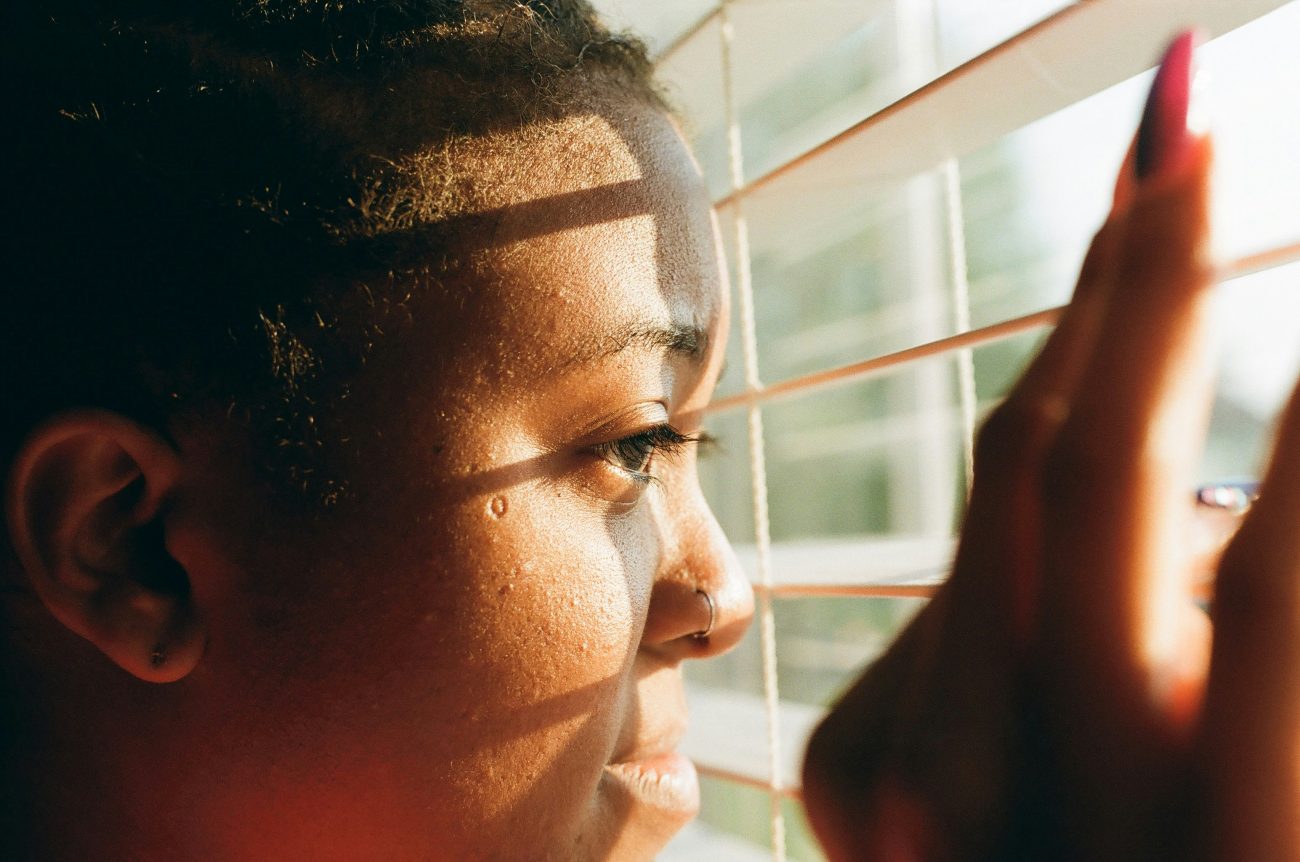 A woman stands alone on her bedroom window, staring outside, symbolizing emotional pain and reflection after a toxic relationship.